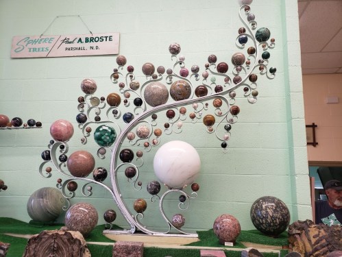 A decorative display of various spherical stones arranged on a tree-like metal structure against a light green wall.