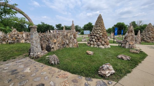 A unique outdoor sculpture garden featuring stone structures and a conical stone formation surrounded by greenery.