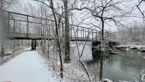 A snowy landscape featuring a bridge over a river, surrounded by bare trees and a snow-covered path.