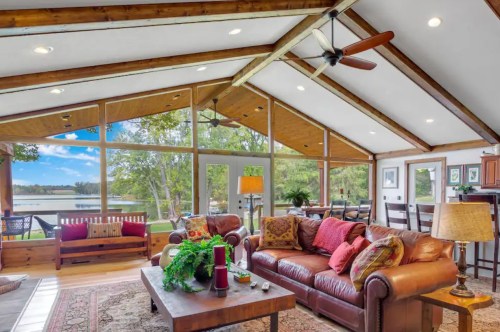 Cozy living room with a lake view, featuring a leather sofa, wooden beams, and large windows.