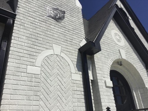 Close-up of a white brick building with decorative architectural elements and a clear blue sky in the background.
