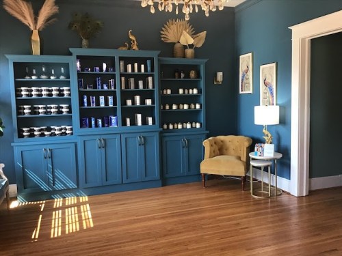 A cozy room with blue walls, a stylish cabinet filled with candles, and a yellow armchair beside a small table.