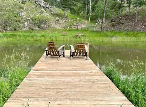 A wooden dock with two chairs overlooks a serene pond surrounded by lush greenery and trees.