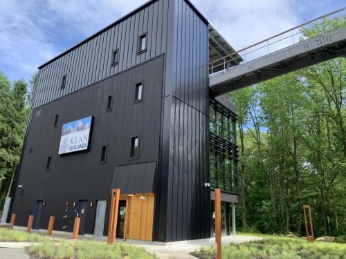 Modern black building with large windows, a sign reading "Kean Skylands," and a walkway above, surrounded by greenery.