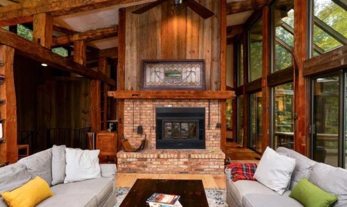 Cozy living room with wooden beams, large windows, a brick fireplace, and comfortable sofas.