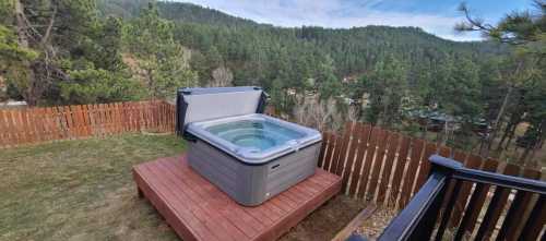 A hot tub on a wooden deck overlooking a forested mountain landscape under a clear blue sky.