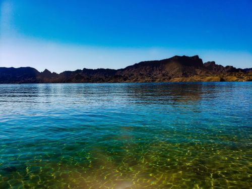 A serene lake with clear turquoise water, surrounded by rocky mountains under a bright blue sky.