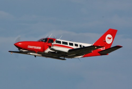 A red and white Coast Guard aircraft flying against a blue sky.