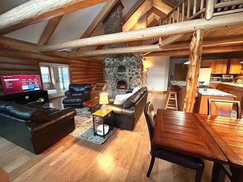 Cozy log cabin interior featuring a stone fireplace, leather sofas, a dining table, and a TV. Warm, inviting atmosphere.