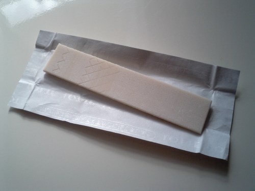A rectangular piece of white candy on a crinkled paper wrapper, with a geometric design etched on its surface.