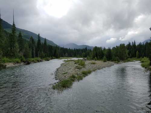 A serene river winding through a lush green landscape under a cloudy sky, surrounded by mountains and trees.