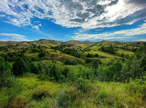 Lush green hills under a blue sky with scattered clouds, showcasing a serene natural landscape.