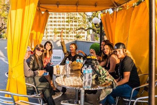 A group of eight friends enjoying drinks and snacks under a yellow canopy, smiling and chatting together.