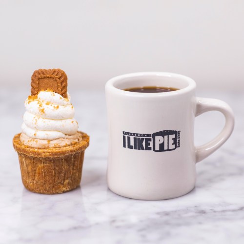 A cupcake topped with whipped cream and a cookie, next to a coffee mug that says "I LIKE PIE."