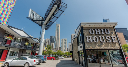 A view of Ohio House with a large billboard and skyscrapers in the background on a clear day.
