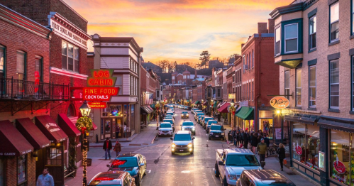 A vibrant street scene at sunset, featuring shops, cars, and people enjoying the lively atmosphere.