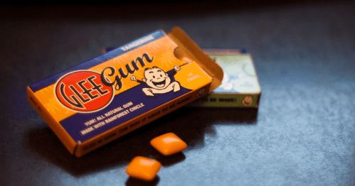 A box of Glee Gum with two orange pieces of gum on a dark surface.
