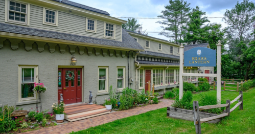 A charming building with a sign reading "Brass Lantern," surrounded by greenery and flower beds.