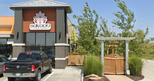 Exterior view of Sakoon The Spa, featuring a sign, parking area, and a landscaped entrance with a wooden gate.