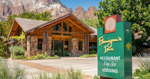 A rustic lodge with a stone facade and wooden beams, surrounded by mountains, featuring a sign for dining and lodging.