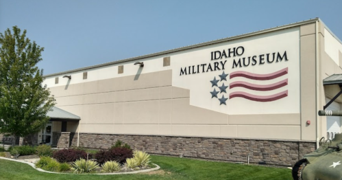 Exterior of the Idaho Military Museum featuring a sign with stars and stripes, surrounded by greenery.