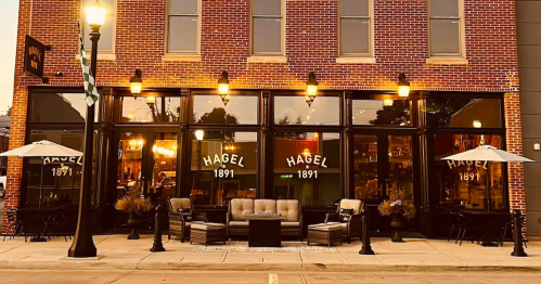 Exterior of Hagel 1891 restaurant with outdoor seating, warm lighting, and a brick facade.