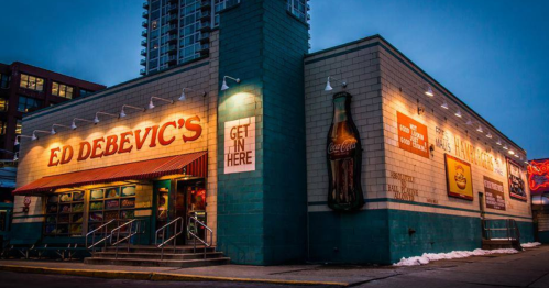 Exterior of Ed Debevic's diner at dusk, featuring neon signs and a vintage Coca-Cola advertisement.