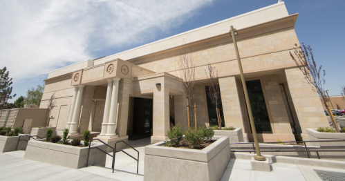 Modern stone building with columns, landscaped planters, and a clear blue sky in the background.