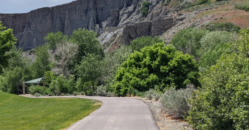 A winding path through lush greenery, with rocky cliffs in the background under a clear blue sky.