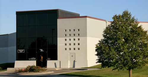 Modern building with a glass facade, white walls, and a small tree in front, set against a clear blue sky.