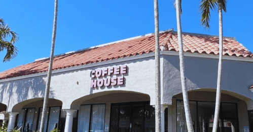 A coffee house with a red-tiled roof, surrounded by palm trees, under a clear blue sky.
