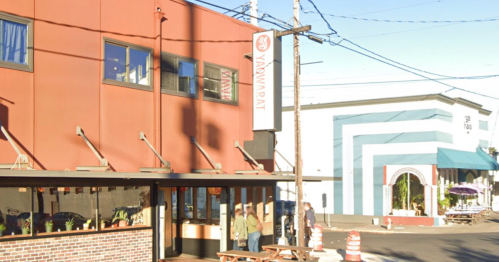 A street view of a restaurant with a red exterior and a sign, next to a blue and white striped building.