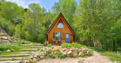 A cozy A-frame cabin surrounded by lush greenery and stone steps, set in a serene natural landscape.