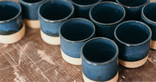A collection of blue ceramic cups with beige bases arranged on a wooden surface.