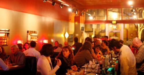 A lively bar scene with patrons enjoying drinks and conversation in a warmly lit setting.