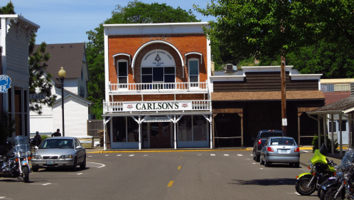 A historic building sits at the end of the road. A large sign that say's "Carlson's" is displayed in front of the building.