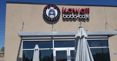 Exterior of Kawa Boba Cafe with a sign and open umbrellas outside. Bright and inviting atmosphere.