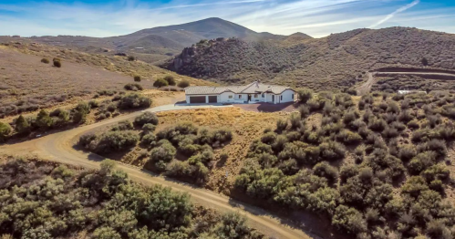 Aerial view of a house surrounded by rolling hills and sparse vegetation on a winding dirt road.