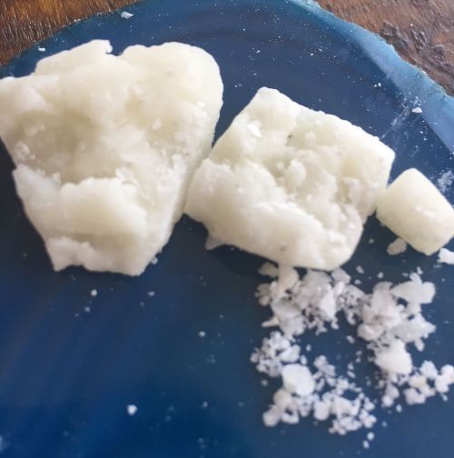 Close-up of white crystalline substance on a blue surface, with larger chunks and fine powder scattered around.
