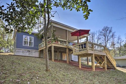 A modern house with a wooden deck and red umbrella, set on a hillside surrounded by trees.