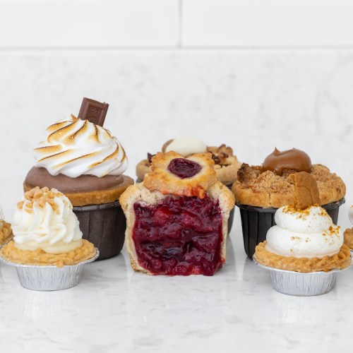A variety of cupcakes and mini pies, featuring flavors like chocolate, cherry, and caramel, on a marble surface.