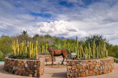 A horse sculpture surrounded by tall cacti and lush greenery under a cloudy sky.