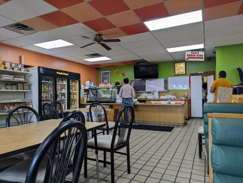 Interior of a casual eatery with tables, a counter, and customers ordering food. Brightly colored walls and a menu display.