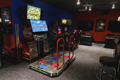 A game room featuring a dance arcade machine, colorful walls, and various arcade games in a cozy setting.