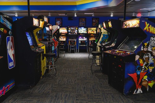 A vibrant arcade filled with classic video game machines and pinball tables, featuring colorful artwork and seating.