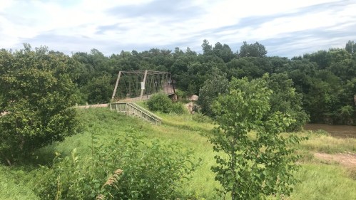 A scenic view of a bridge over a river, surrounded by lush greenery and trees under a cloudy sky.