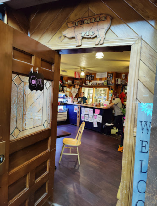A cozy café entrance with a wooden door, welcoming sign, and a glimpse of the interior and staff at the counter.