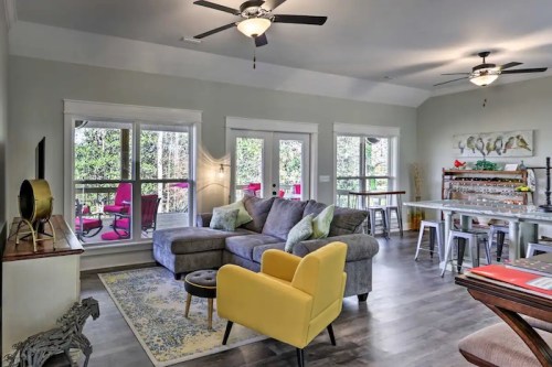 Cozy living room with a gray sectional, yellow chair, and large windows overlooking a green outdoor space.