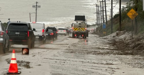 Traffic on a flooded road with debris, a fire truck, and a warning sign about potential flooding.