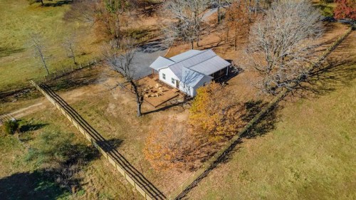 Aerial view of a white house surrounded by trees and a wooden fence in a grassy landscape during autumn.